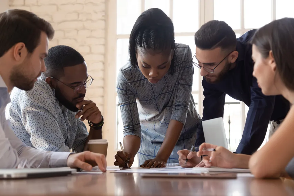 Focused arican american millennial female team leader leaned over table