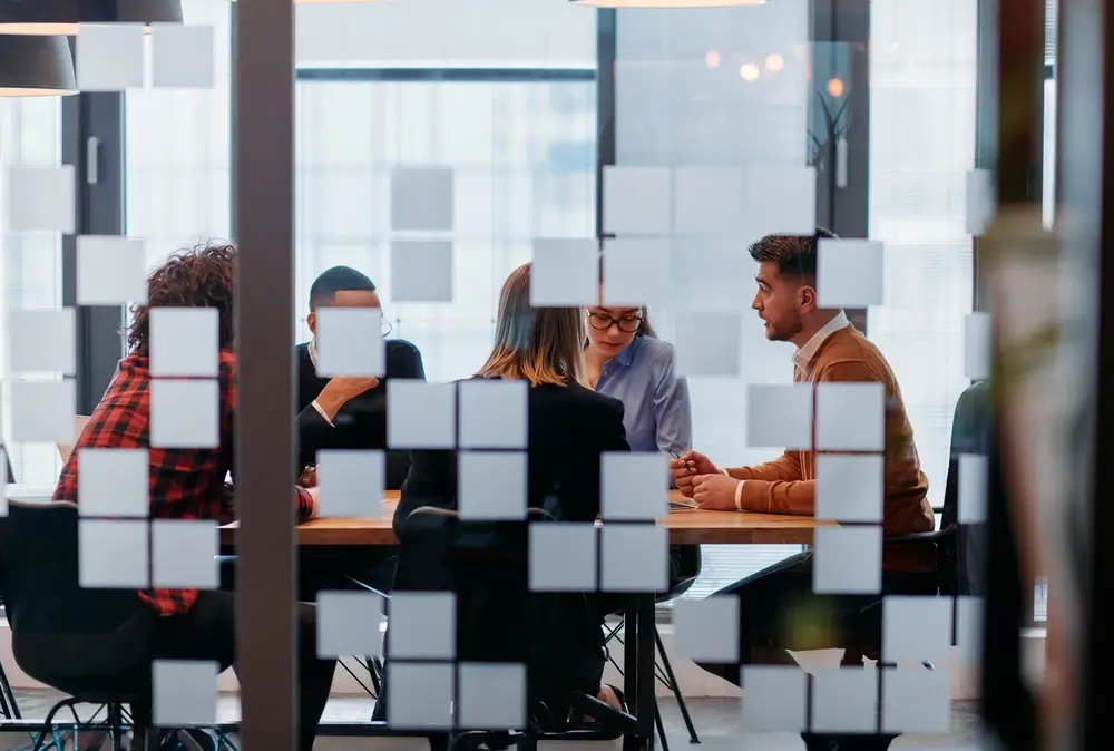 In a sleek glass office space, a team of business professionals engage in lively discussions and exchange strategic ideas